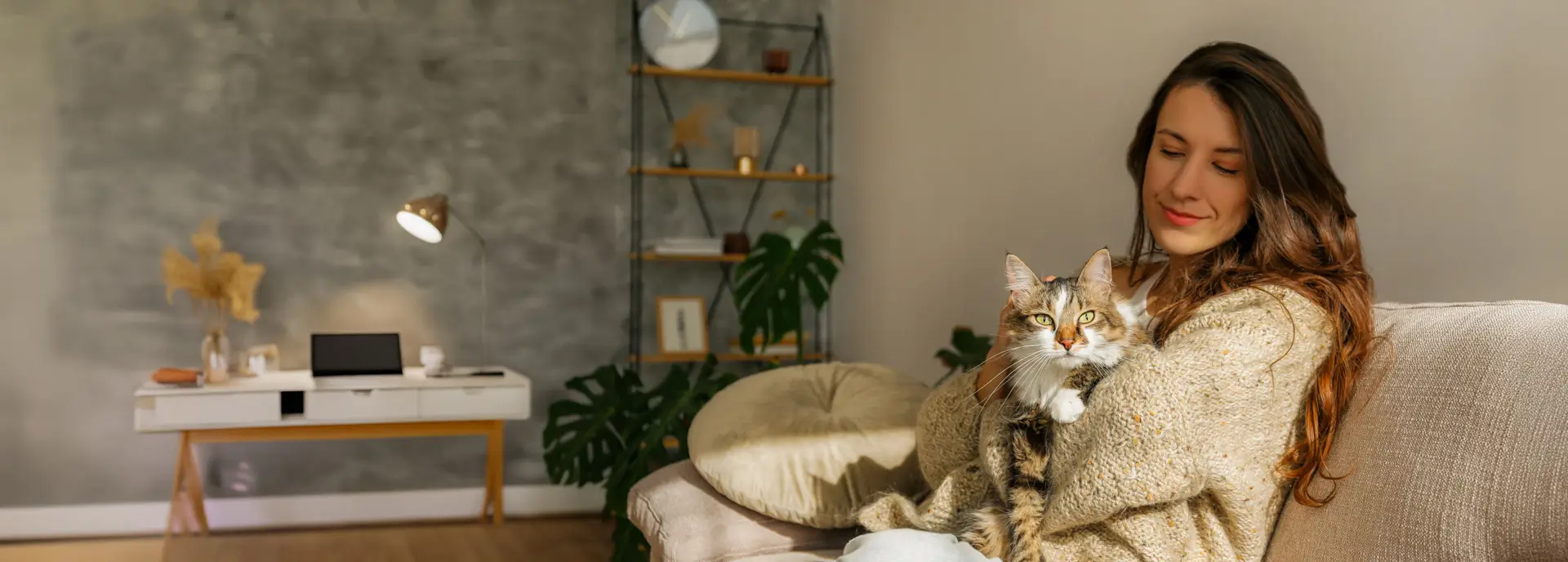 A woman smiles as she sits comfortably on her couch and holds her cat