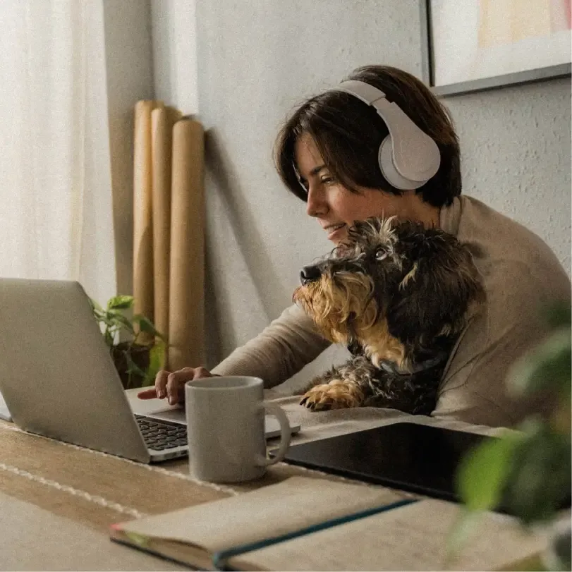 A young woman listens to her headphones while working as her dog looks on